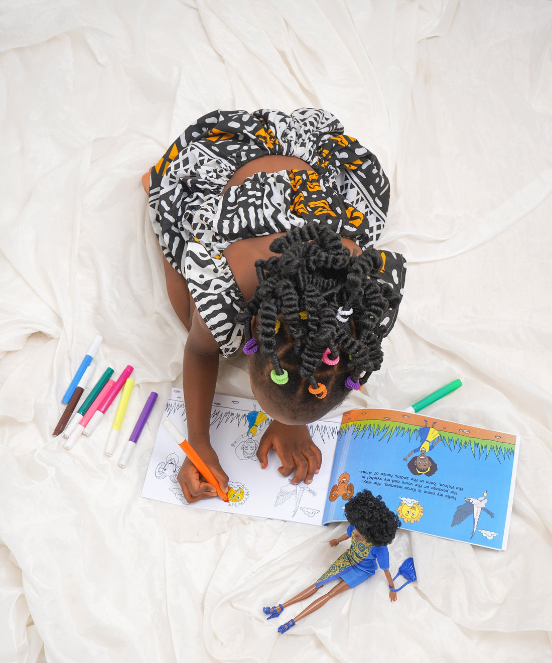 Young Black girl coloring beside The Nubian Princesses book and doll, showcasing cultural representation in play and learning.