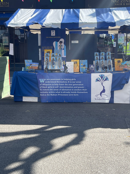 Outdoor Nubian Princesses stall displaying Black dolls and children's books that celebrate representation, identity, and empowerment.